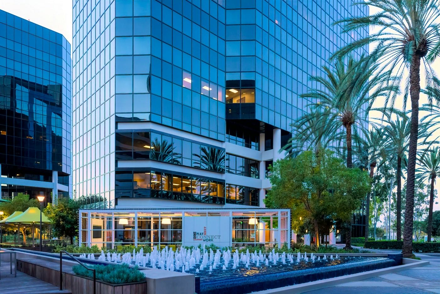 Glass office towers, palm trees and a fountain in the Irvine business district at dusk