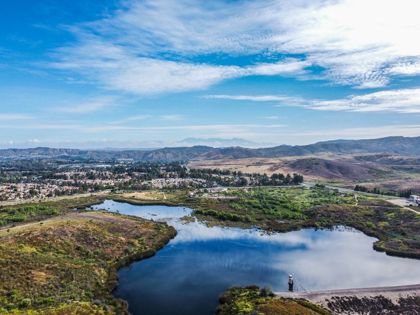 A lake among green hills with neighborhoods and mountains in the distance