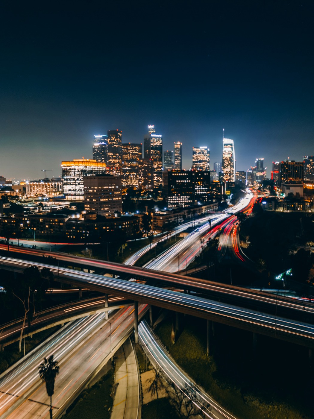 Light trails on a freeway interchange in front of the downtown Los Angeles skyline at night