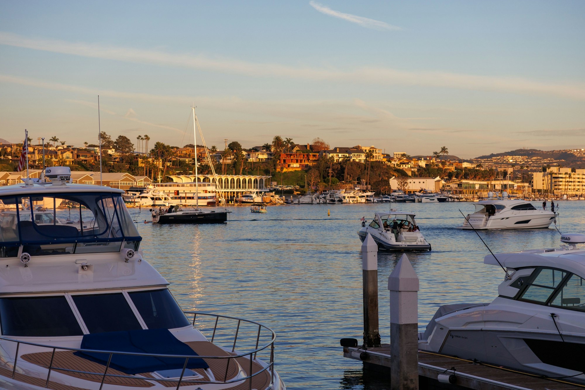 Yachts in Newport Harbor at golden hour with hillside homes behind