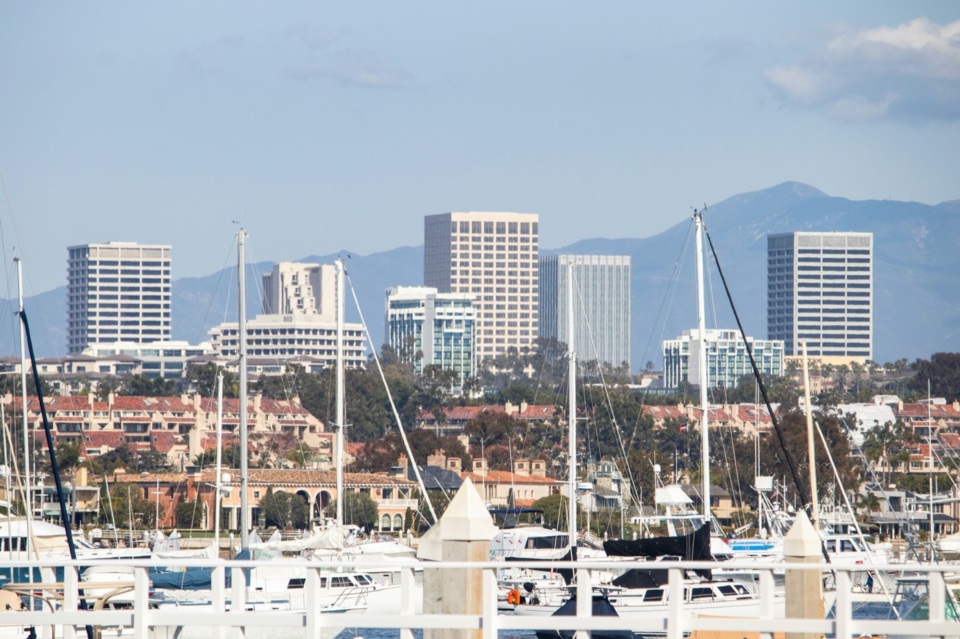 Sailboat masts in Newport Harbor with the office towers of Newport Center and the mountains behind