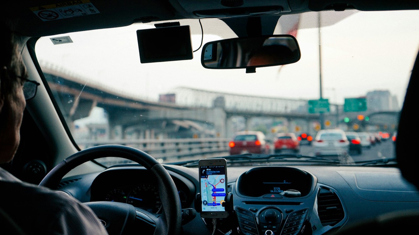 A phone on a dashboard mount showing turn-by-turn navigation in city traffic