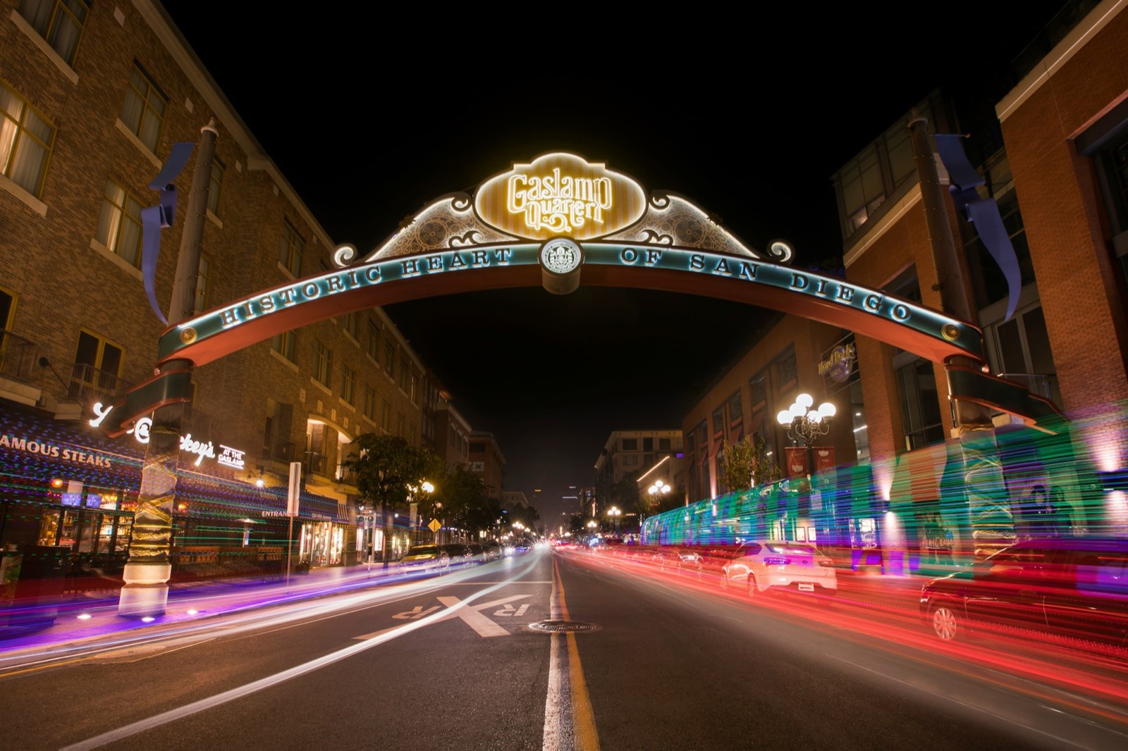 The lit Gaslamp Quarter sign arching over Fifth Avenue at night with light trails