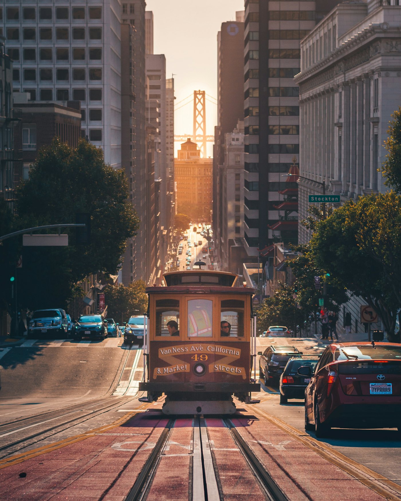 A San Francisco cable car climbing California Street with the Bay Bridge at sunset behind it
